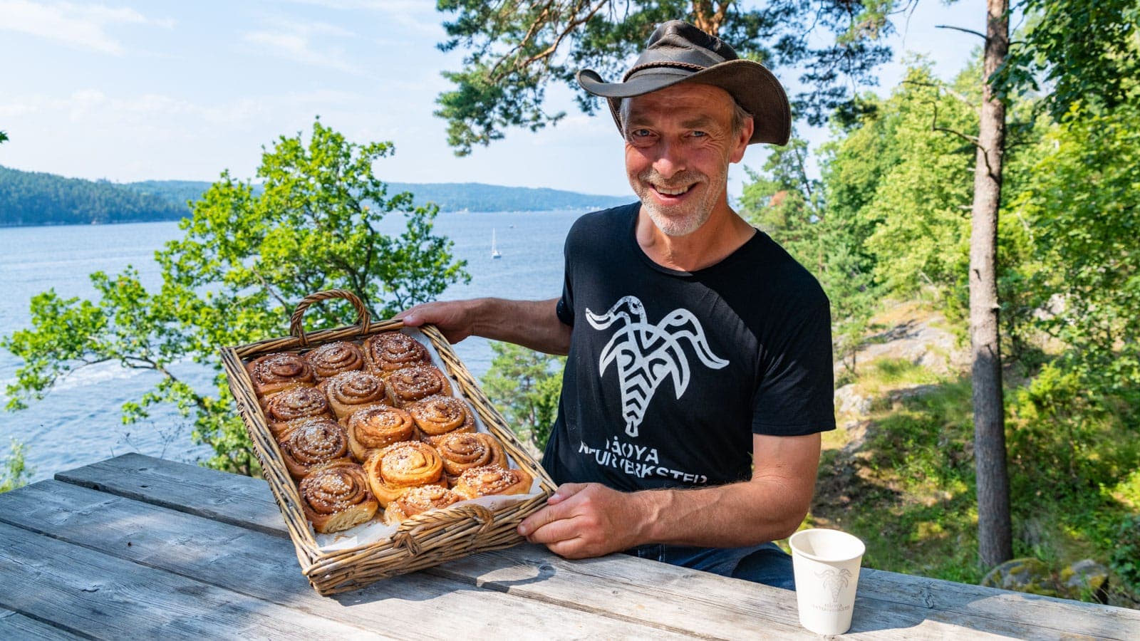 Mann med hatt som holder kanelboller med fjorden i bakgrunn