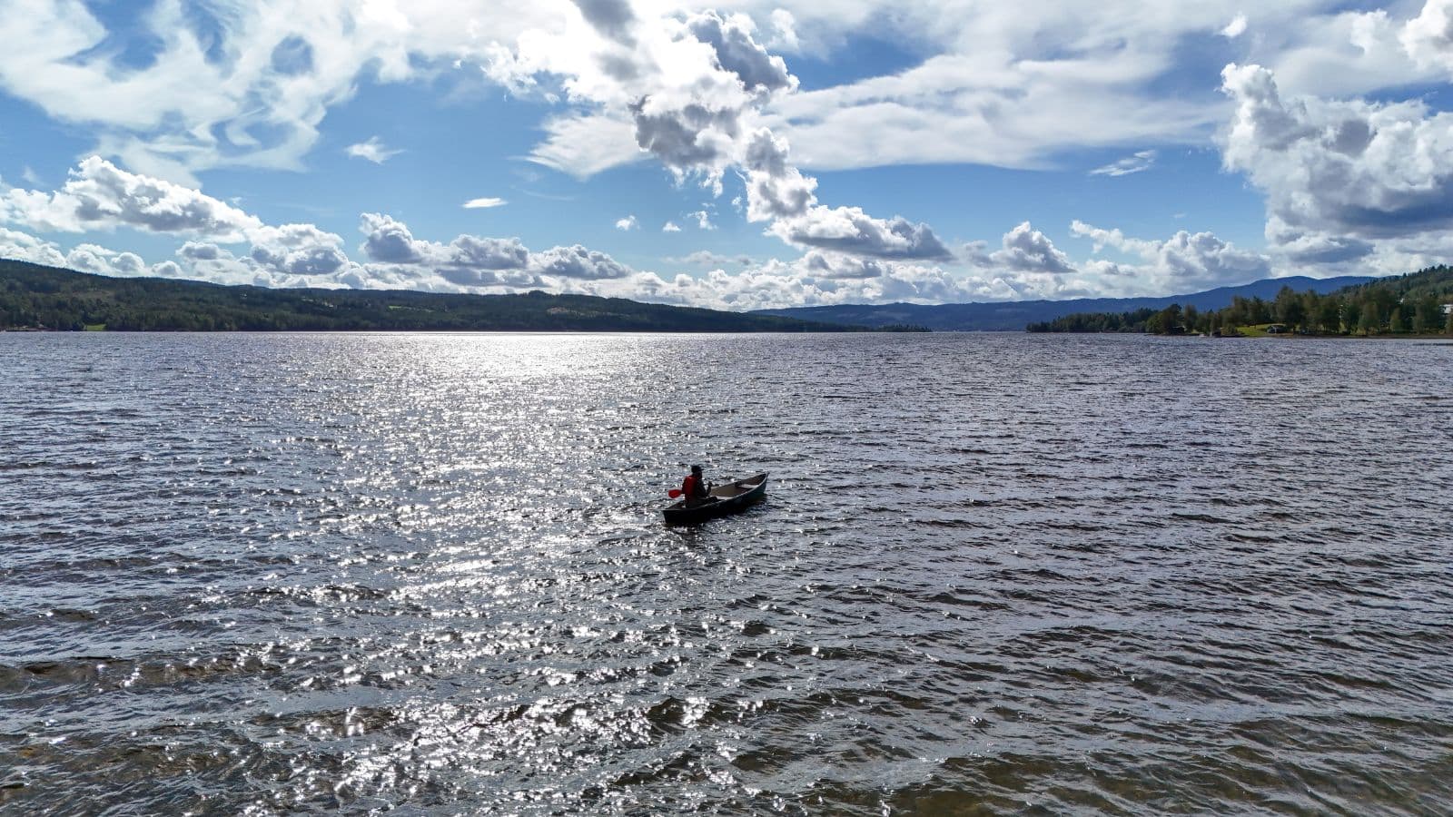 person i båt på en innsjø omgitt av skog og fjelltopper