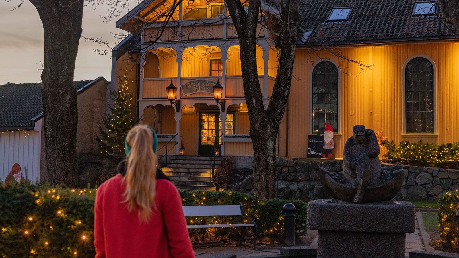 Dame som står utenfor et gult trehus med julelys